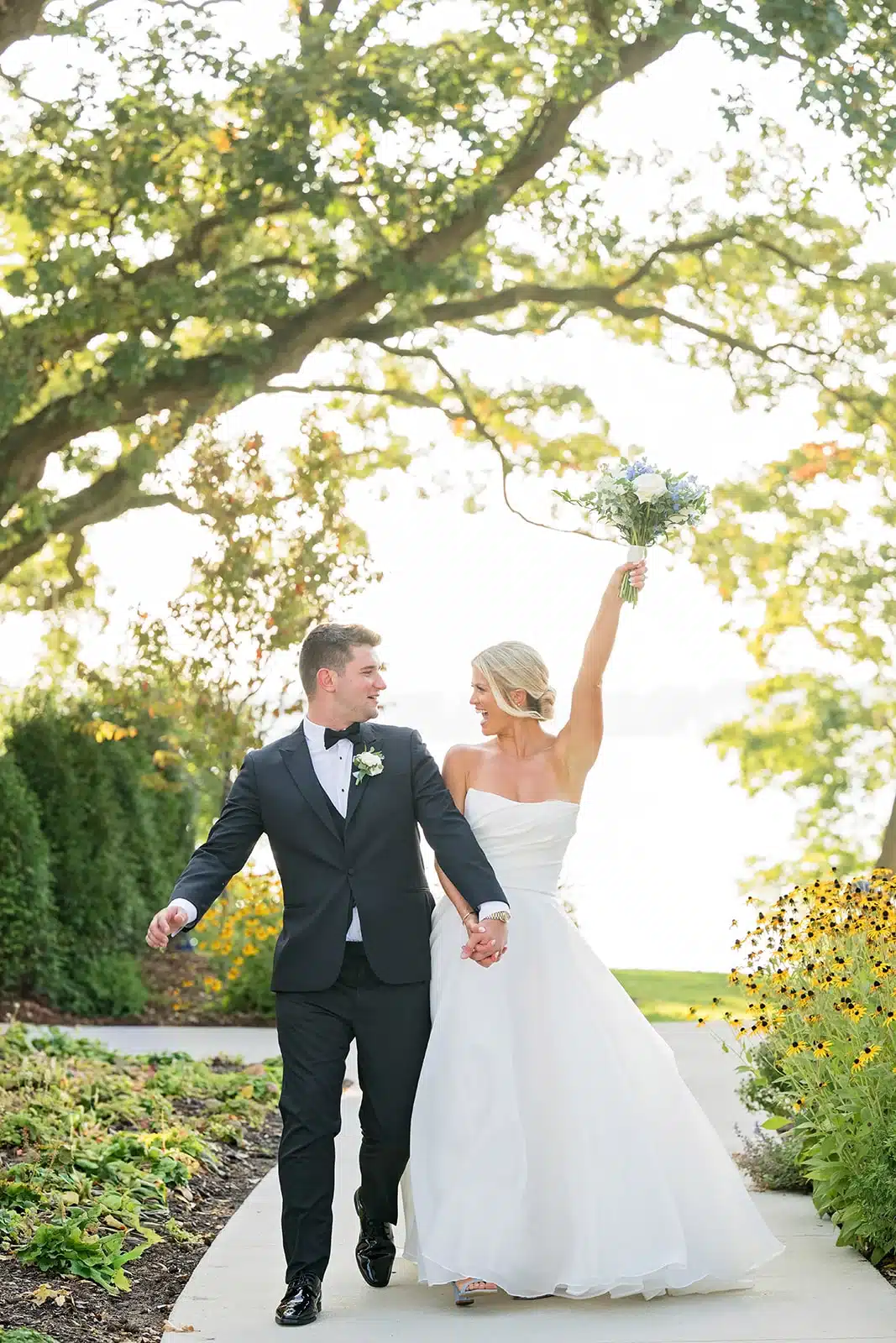 Bride and groom walking hand in hand as she throws her bouquet up with Nagawicka Lake in the background at The Commodore. Bride and groom walking hand in hand as she throws her bouquet up with Nagawicka Lake in the background at The Commodore.