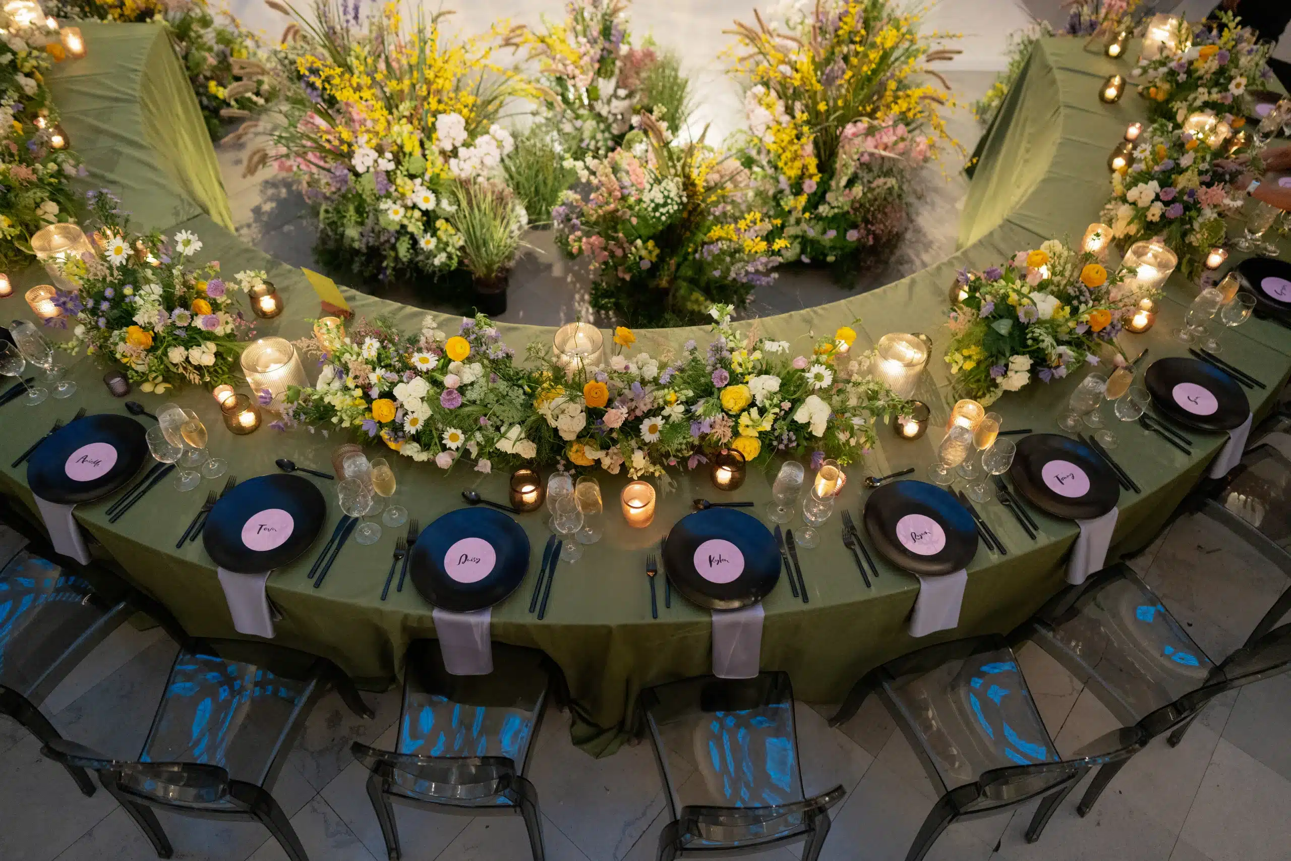 Serpentine Table with green linens, soft pink flowers and colorful dinnerware by Estera Events. 2026 Event Rental Tablescapes & Trends