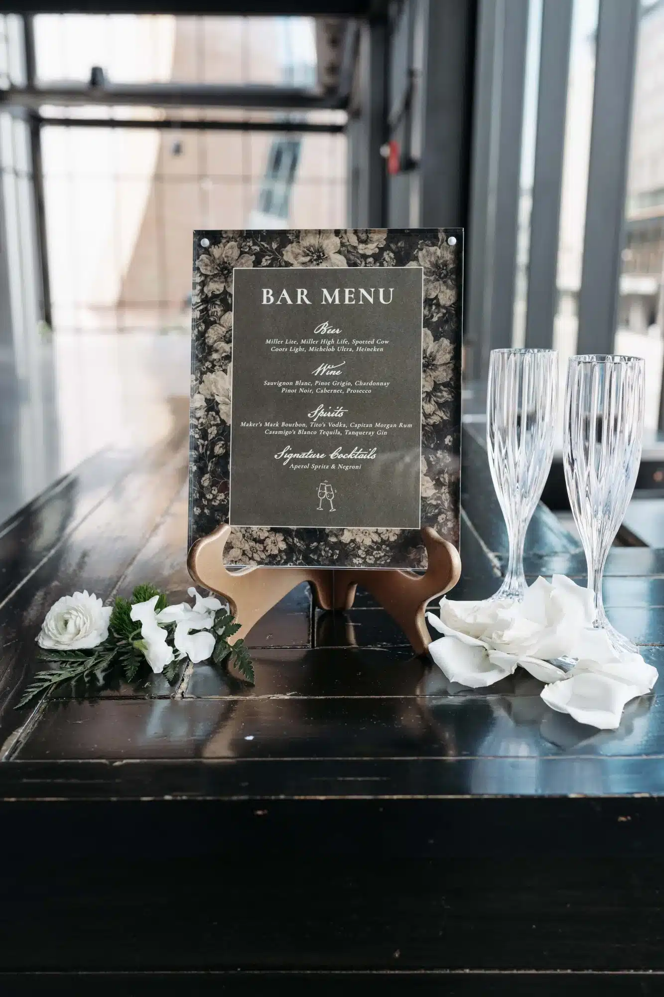 Classy black and tan floral bar menu placed in acrylic frame on gold stand. Classy black and tan floral bar menu placed in acrylic frame on gold stand.