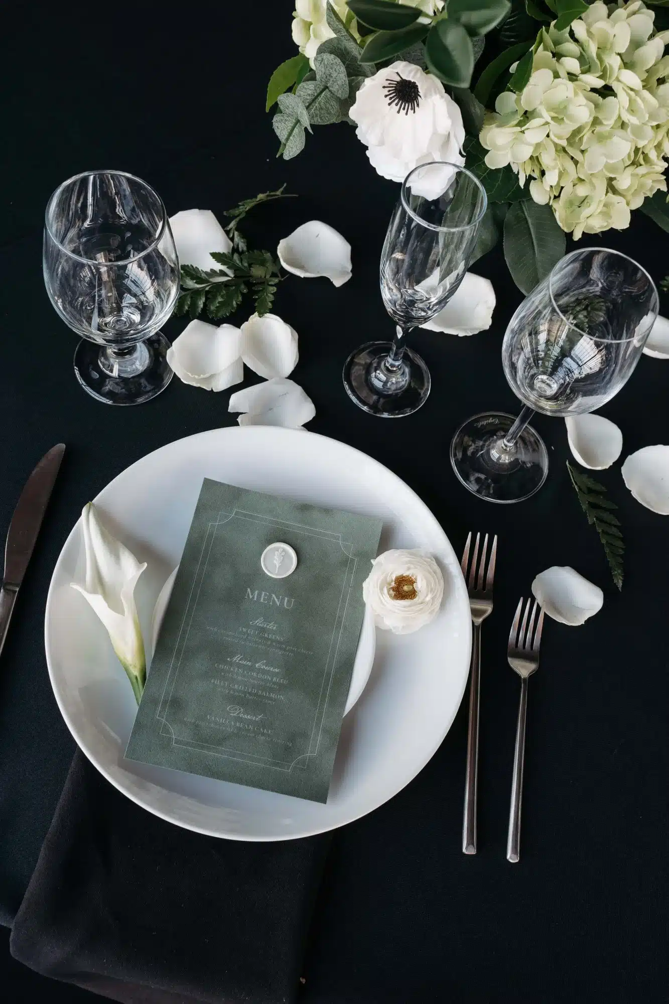 Wedding table setting with black table cloth, green menus, white plates and white floral accents. Wedding table setting with black table cloth, green menus, white plates and white floral accents.