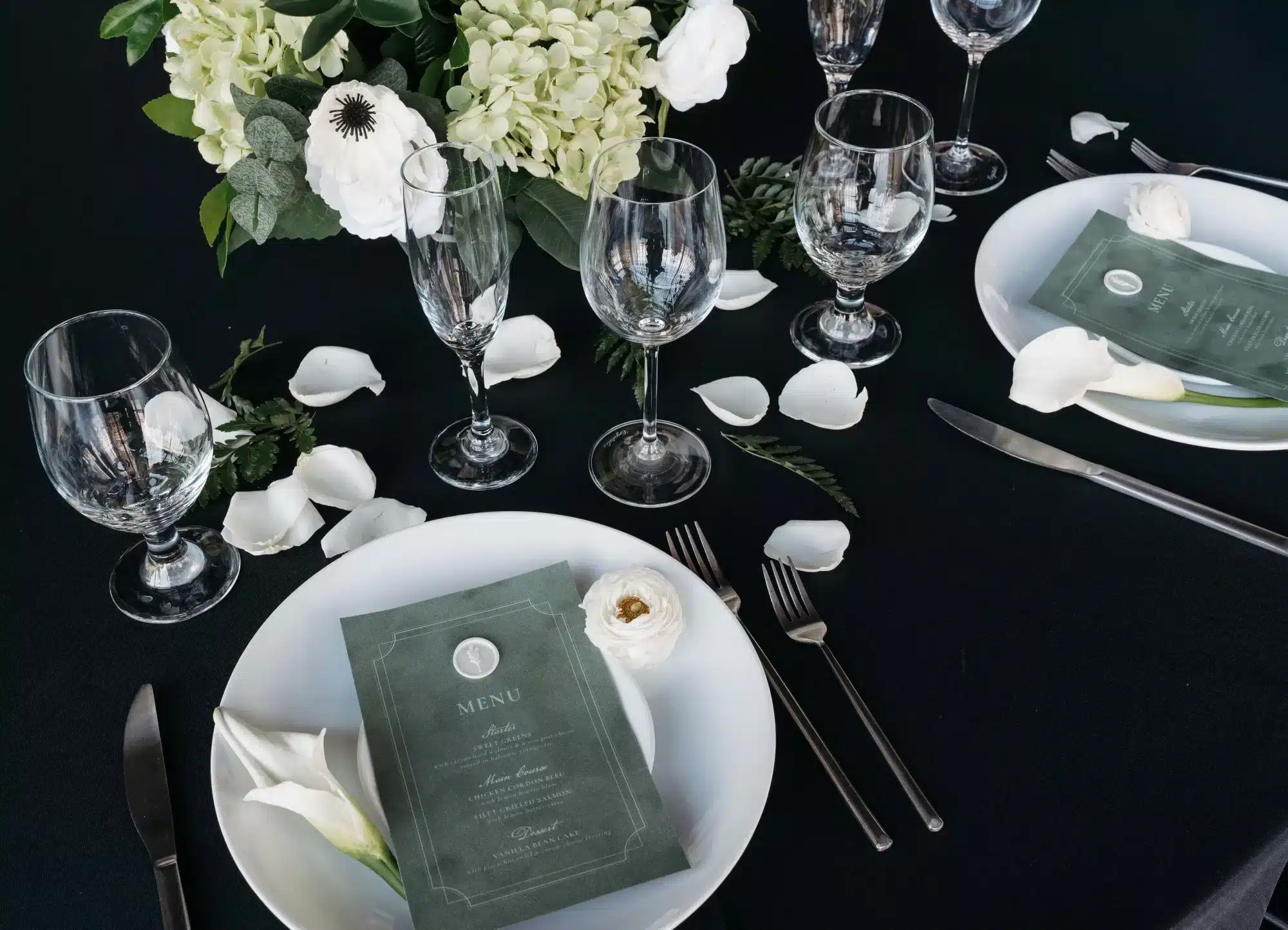 Wedding table setting with black table cloth, green menus, white plates and white floral accents. Wedding table setting with black table cloth, green menus, white plates and white floral accents.