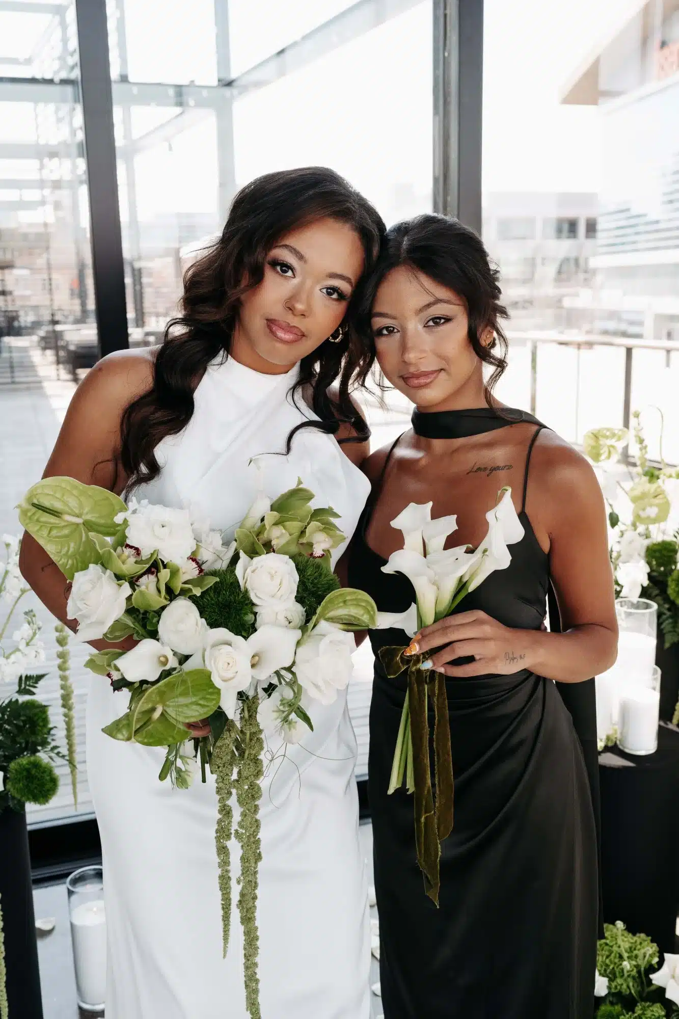 Bride in halter neck gown stands next to bridesmaid in olive green dress. Bride in halter neck gown stands next to bridesmaid in olive green dress.