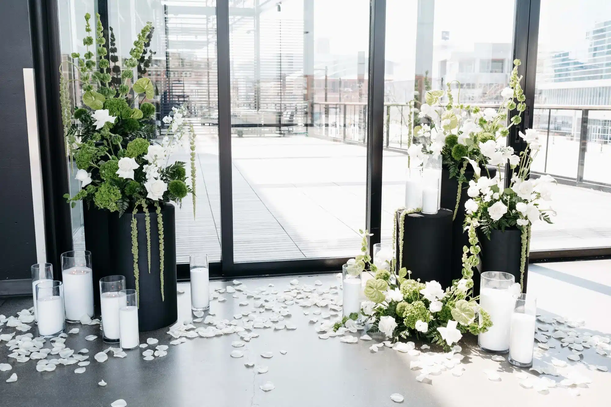 Floral arrangement setup for ceremony backdrop with tall greenery and white flowers, large candles and black pedastals. Floral arrangement setup for ceremony backdrop with tall greenery and white flowers, large candles and black pedastals.