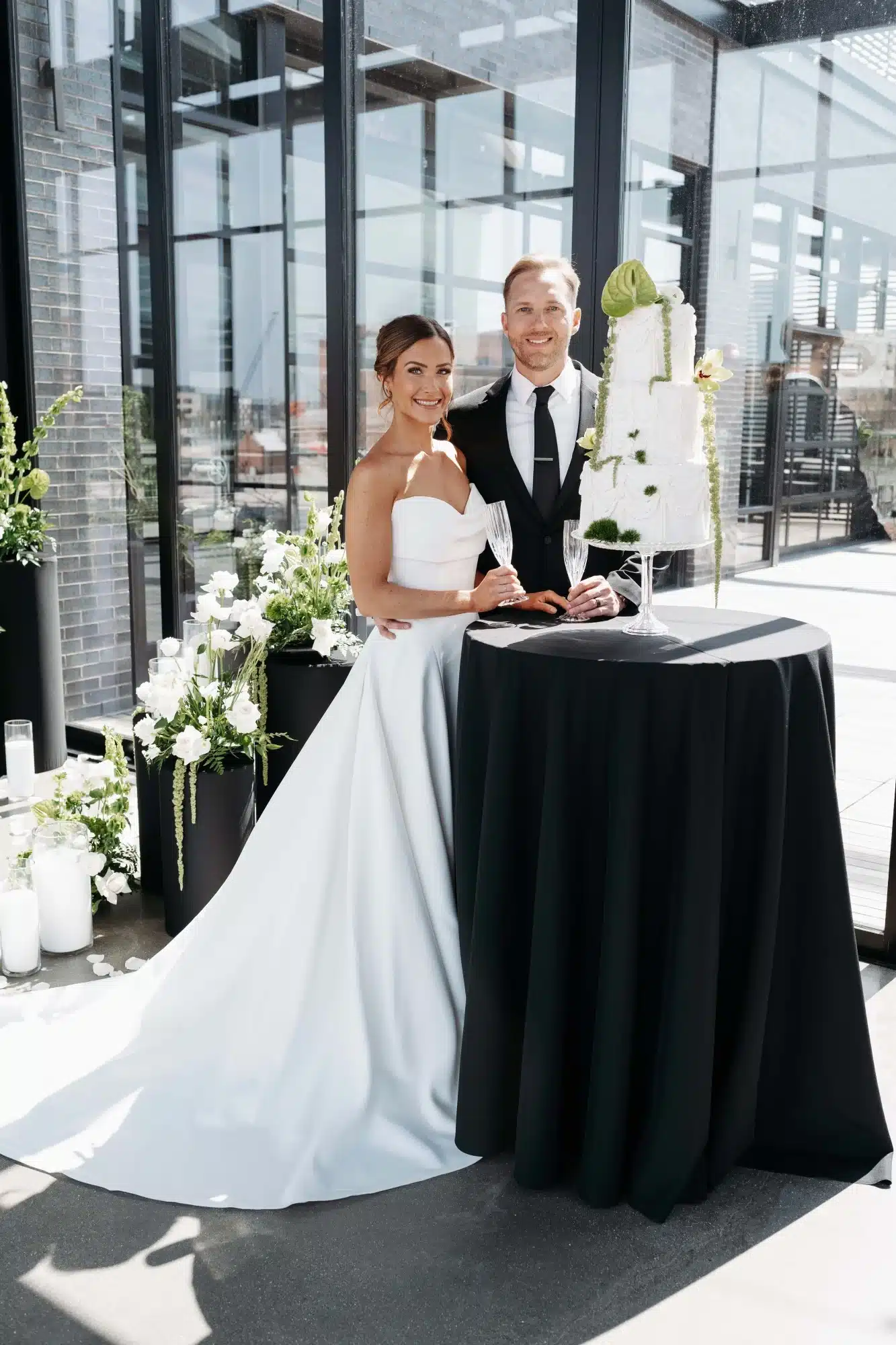 Bride and groom stand next to three tier white cake from Whisk Chick. Bride and groom stand next to three tier white cake from Whisk Chick.