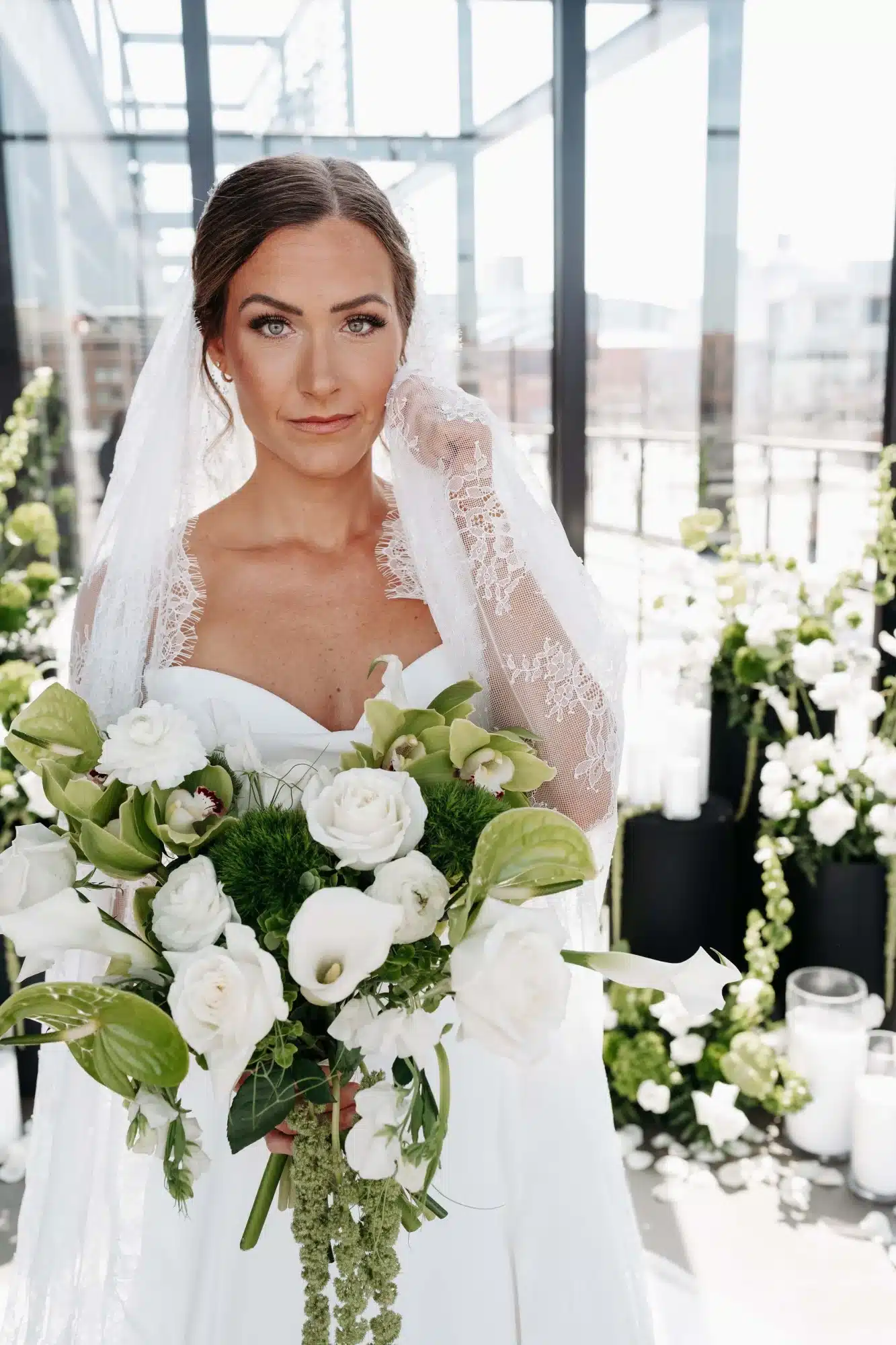 Bride with a sleek updo and lace veil holding white and greenery bouquet wearing a strapless gown. Bride with a sleek updo and lace veil holding white and greenery bouquet wearing a strapless gown.