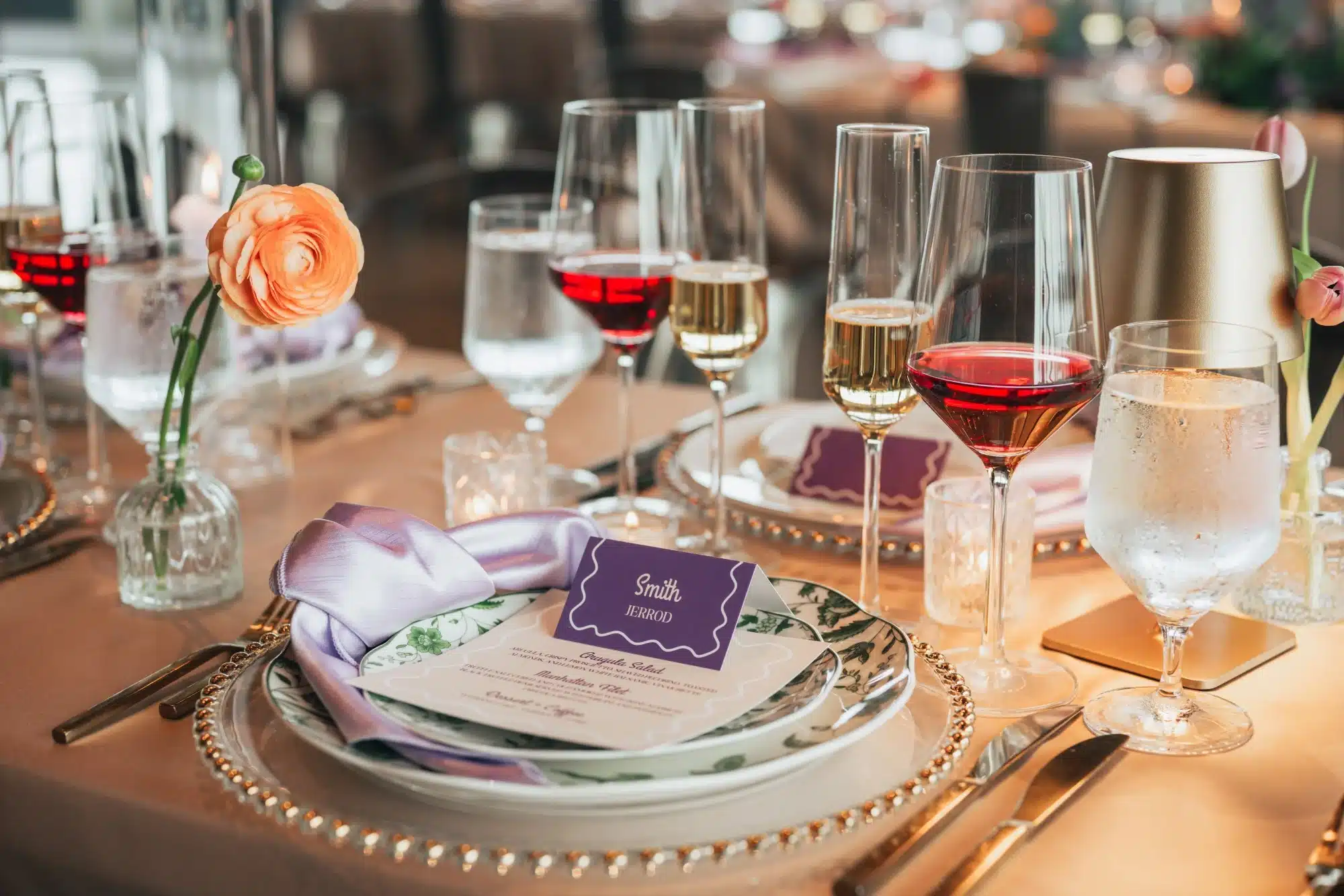 Place setting with wine glasses, green floral vintage plates, gold beaded chargers and purple napkin and placecard. Place setting with wine glasses, green floral vintage plates, gold beaded chargers and purple napkin and placecard.