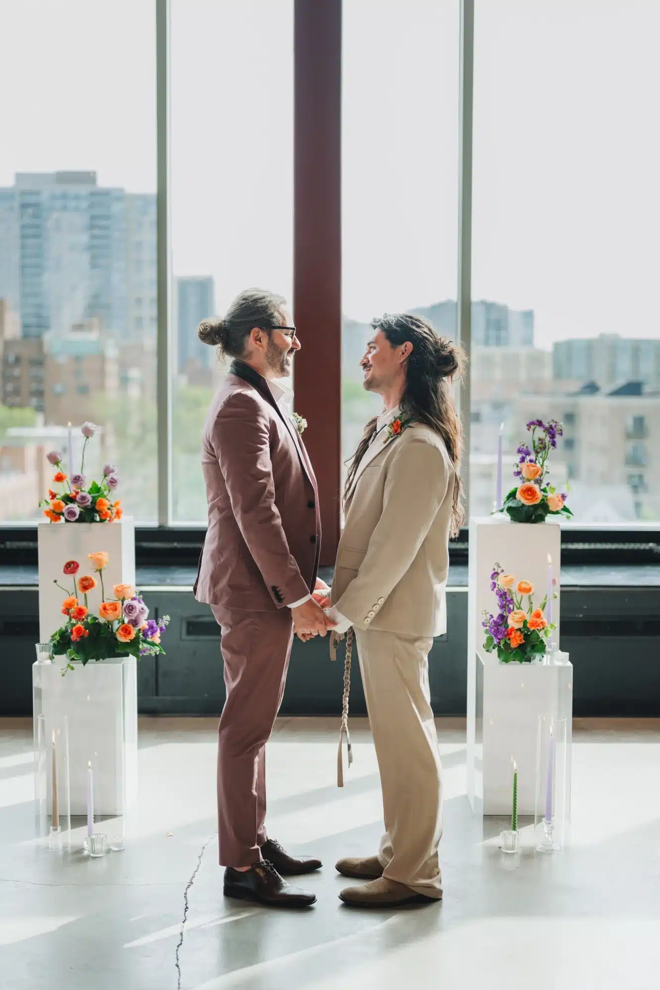 Grooms look into each others eyes at wedding ceremony of white pillars and colorful flower arrangements. Grooms look into each others eyes at wedding ceremony of white pillars and colorful flower arrangements.