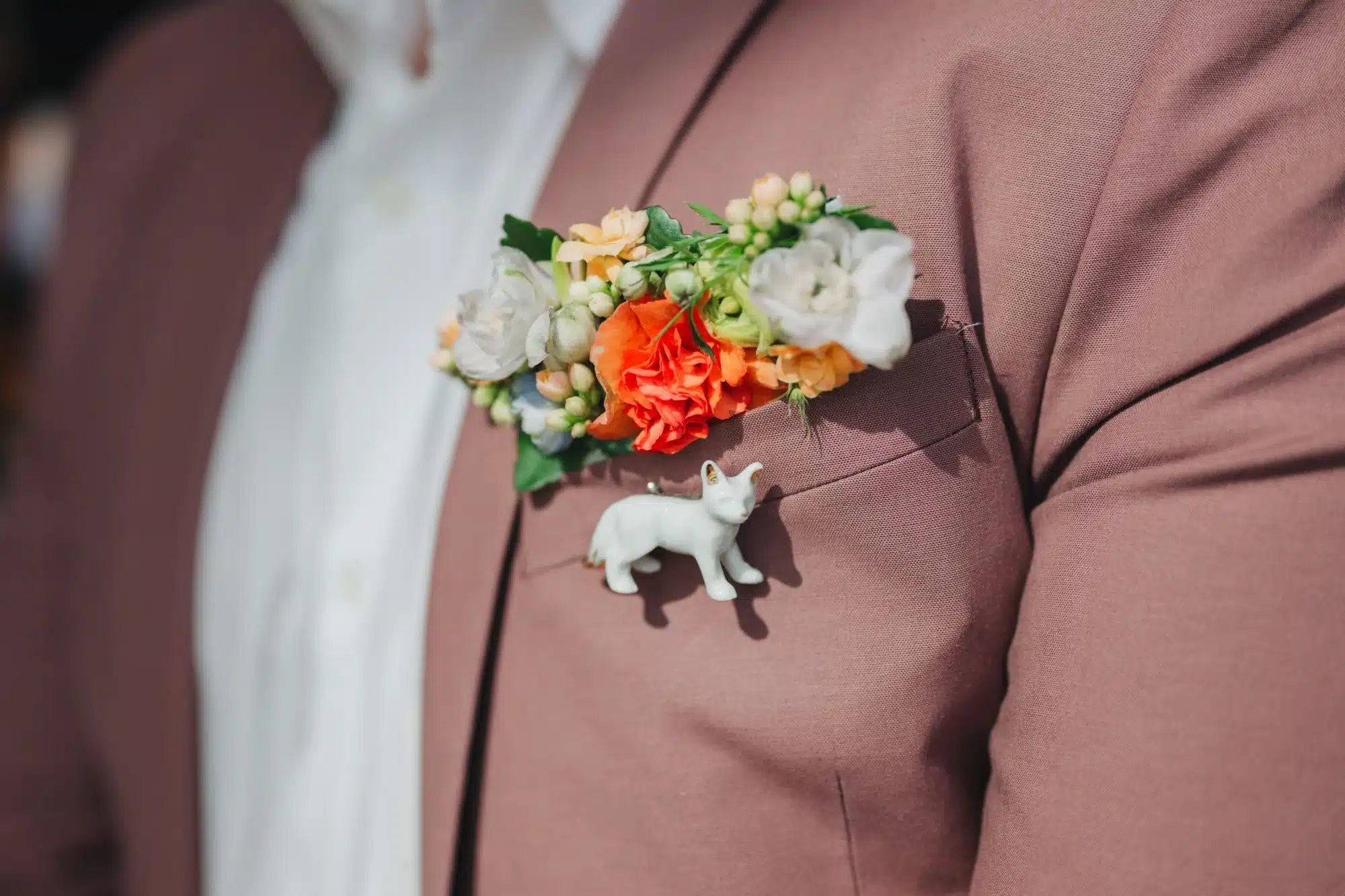 Pocket boutonniere with white, orange and coral flowers with a cat porcelain pin hanging below. Pocket boutonniere with white, orange and coral flowers with a cat porcelain pin hanging below.
