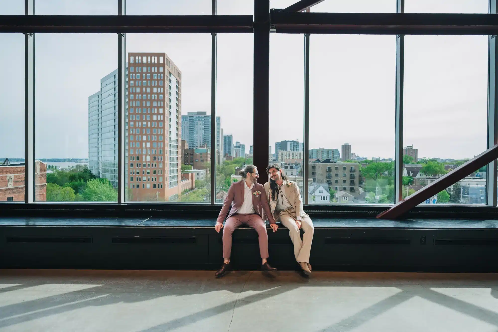 Grooms sitting on the ledge seating of Jan Serr Studio, one in a tan suit and the other in mauve. Grooms sitting on the ledge seating of Jan Serr Studio, one in a tan suit and the other in mauve.