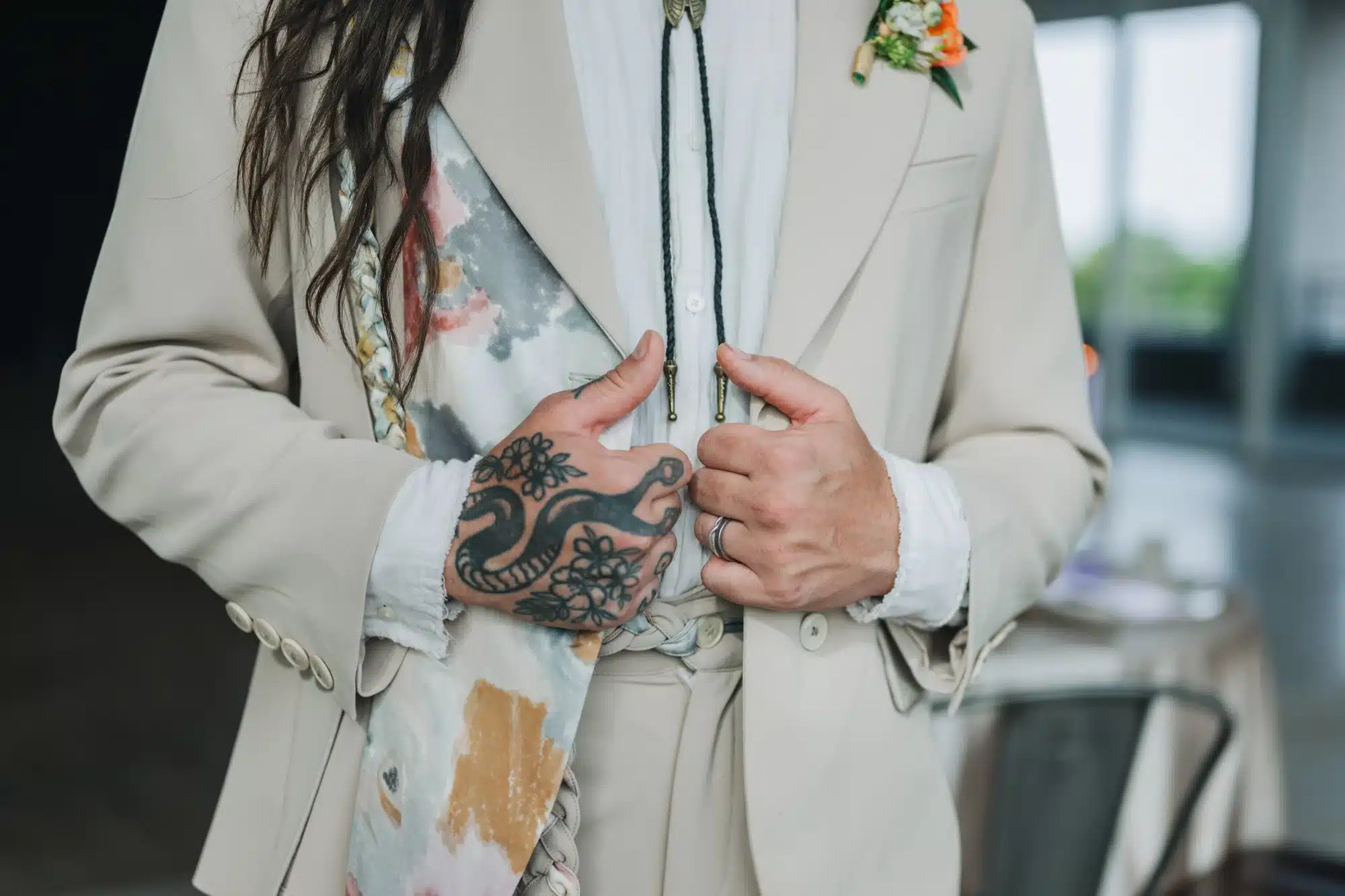 Close up photo of groom wearing tan suit, tattoos on hand with colorful scarf. Close up photo of groom wearing tan suit, tattoos on hand with colorful scarf.
