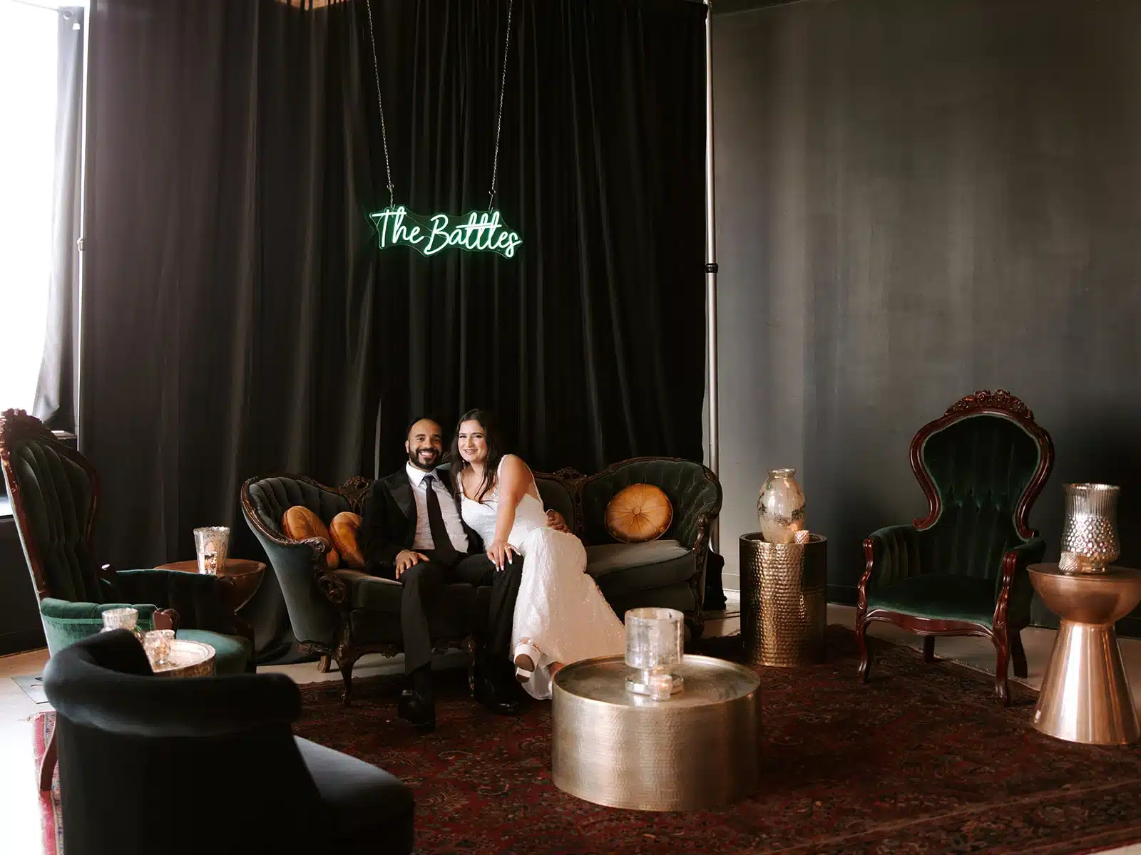 Bride and groom sitting in lounge area with their name in displayed on a neon sign.