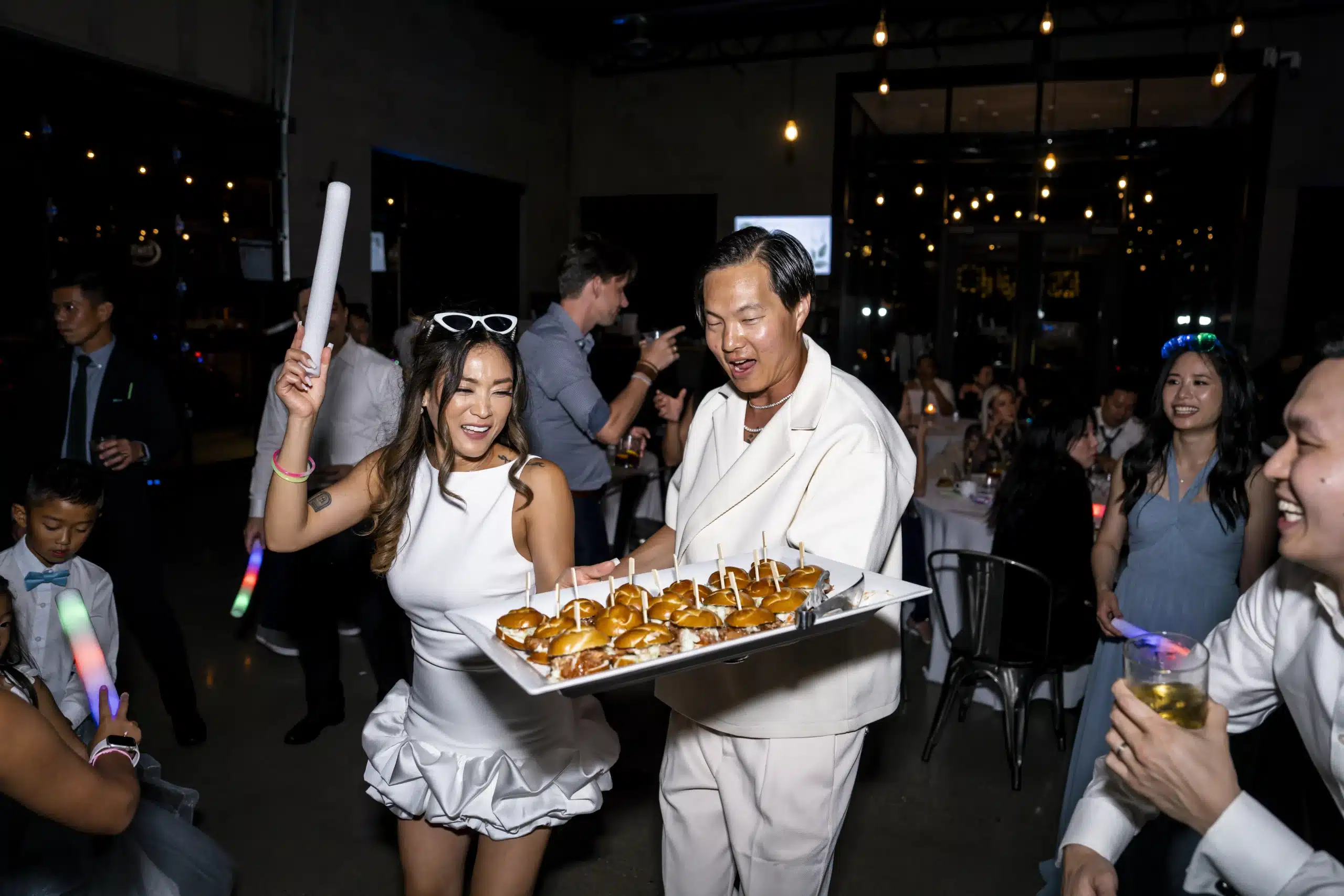 Bride and groom dance at their reception celebrating and holding a plate of sliders.