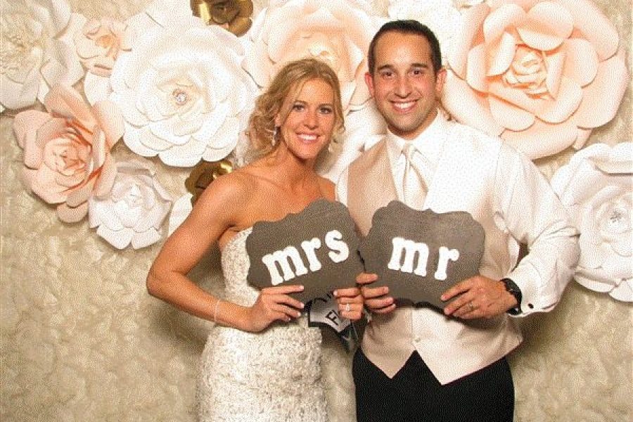 Bride and groom in front of flower backdrop holding Mr. and Mrs. sign