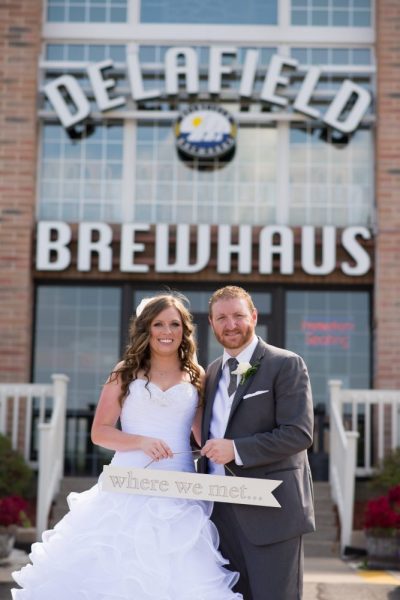 Bride and groom holding sign that says Where we met in front of the Delafield Brewhaus
