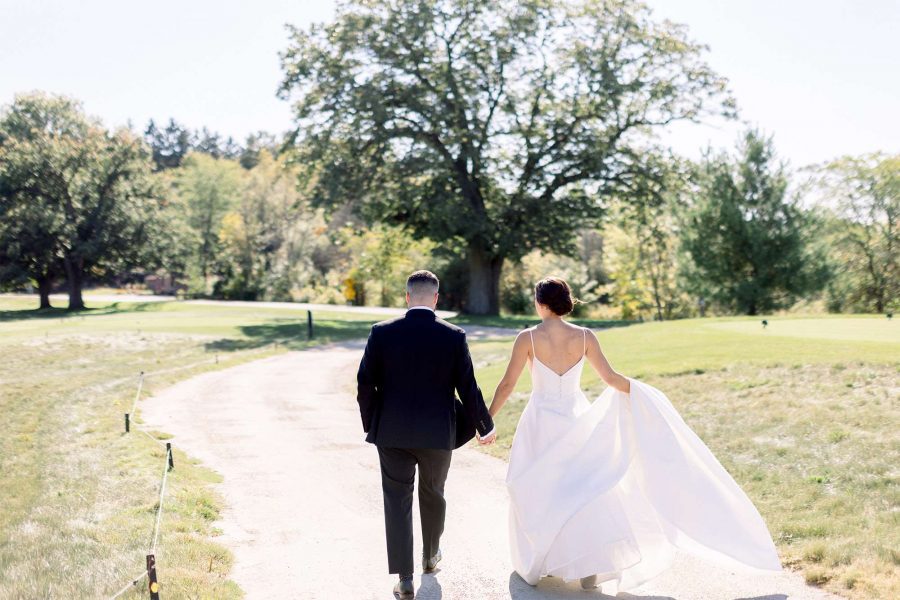 Bride and groom walk hand in hand up path at the Club at Lac La Belle.