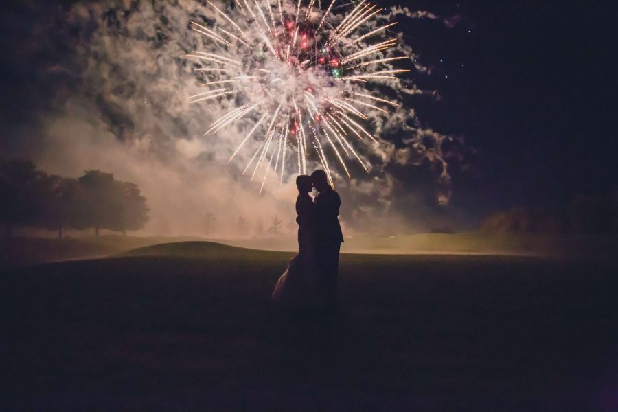 Fireworks in background with wedding couple hugging in forefront at Clubhouse at the Bog wedding