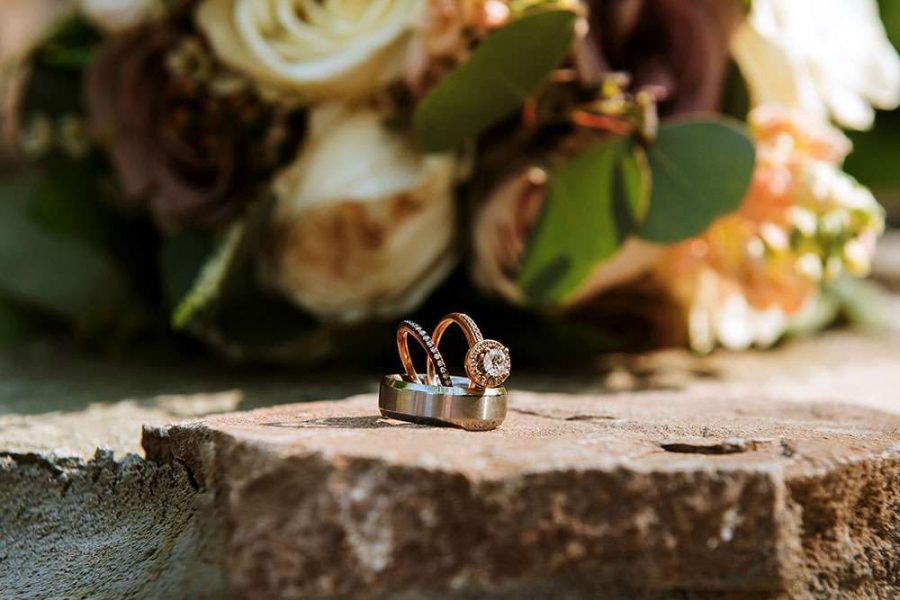 Wedding-rings beautifully place on tree stub with bridal bouquet in background