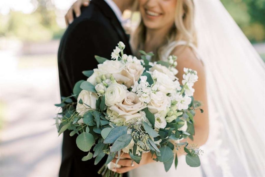 Large wedding bouquet with white roses and greenery accents. Close up shot with couple in the background. flowers done by Bank of Flowers in Wisconsin.