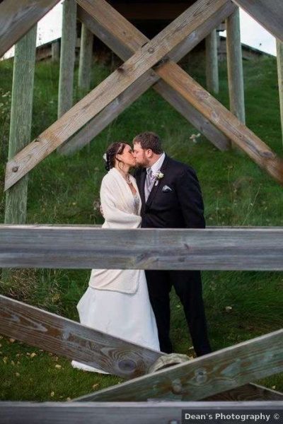 Bride and groom kiss under wooden bridge