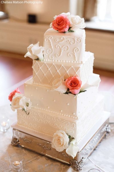 Elegant white wedding cake by Sweet Perfections Bake Shoppe adorned with white and pink flowers.