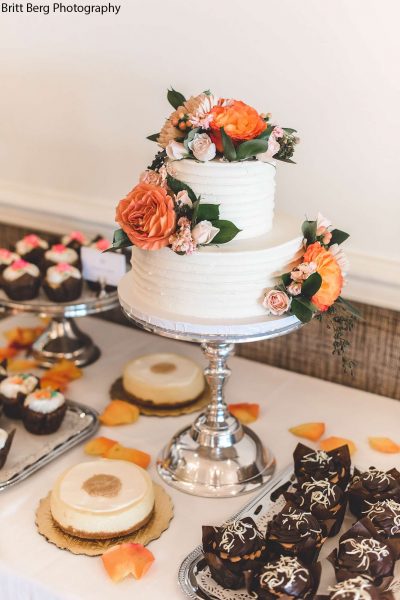 2 tiered white wedding cake adorned with tangerine hued flowers on a sweet table.