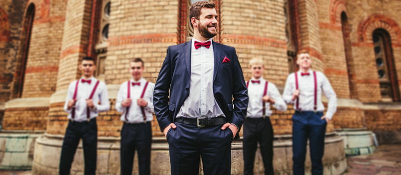 groom with red bowtie standing in front of groomsmen wearing suspenders