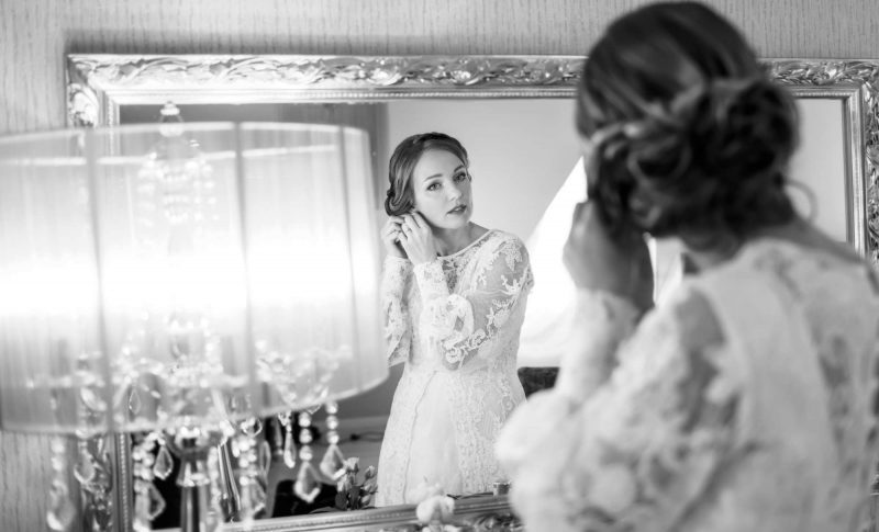 black and white photo, bride getting ready, bride looking in mirror putting on earrings
