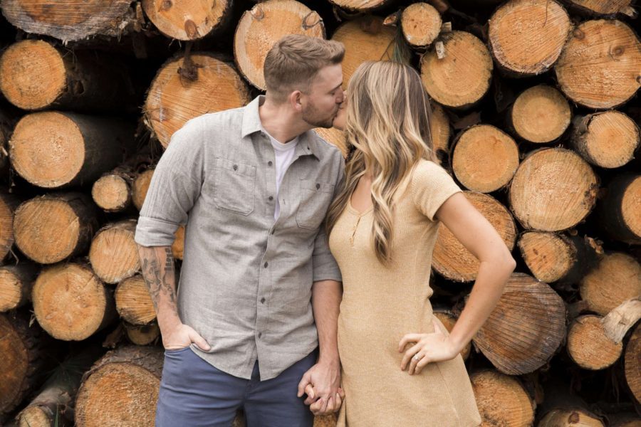 Engagement image of couple by log pile by Wild Elegance Photography