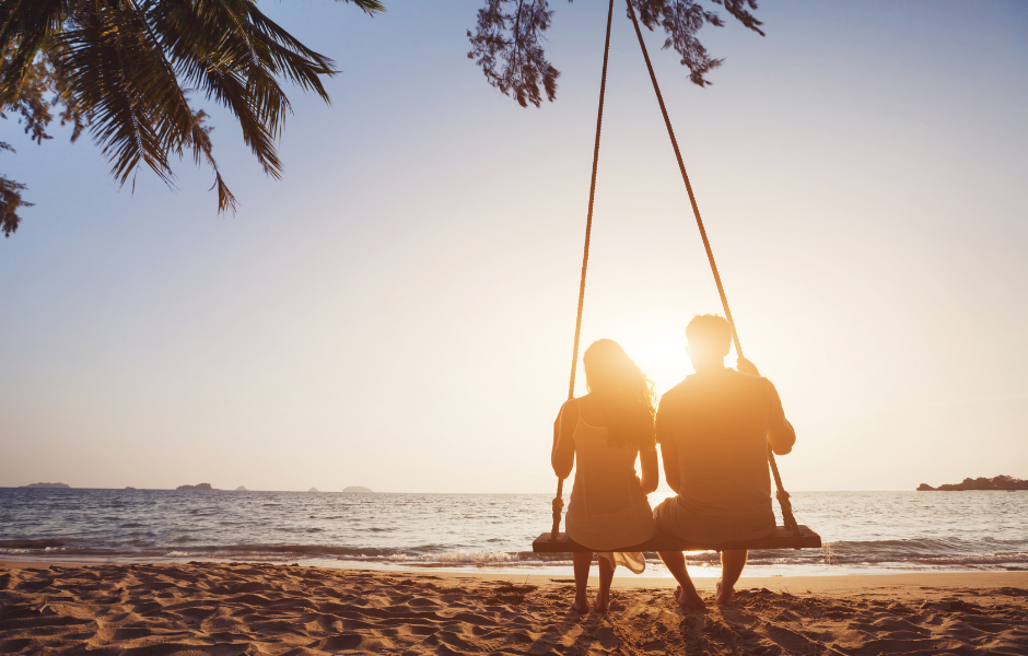 Couple sit on swing at sunset on the beach