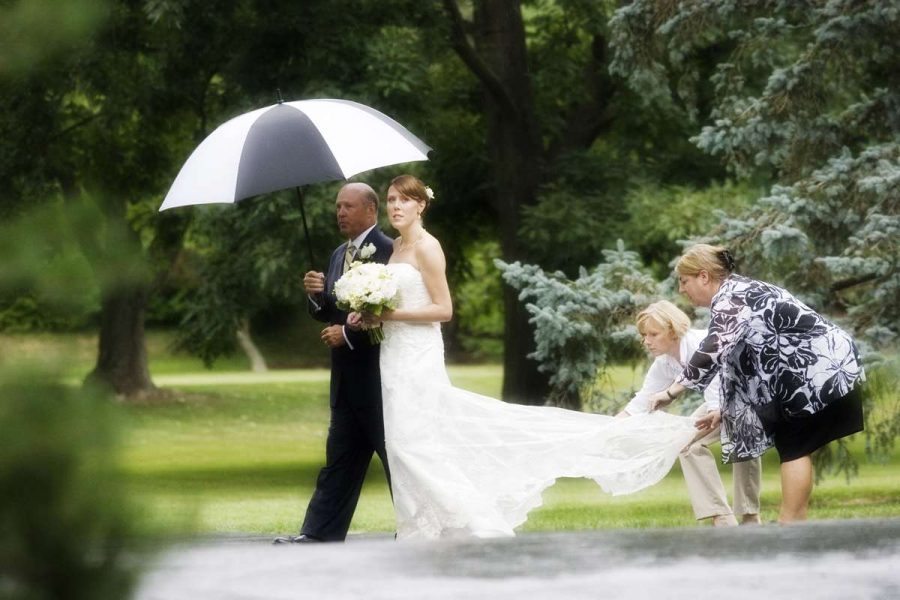 Bride under umbrella prepares to walk down outdoor wedding ceremony aisle