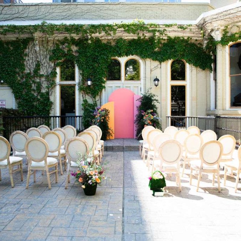 Outdoor ceremony space at The Fitzgerlad with colorful backdrop arches and white fabric chairs, ivy up the walls.