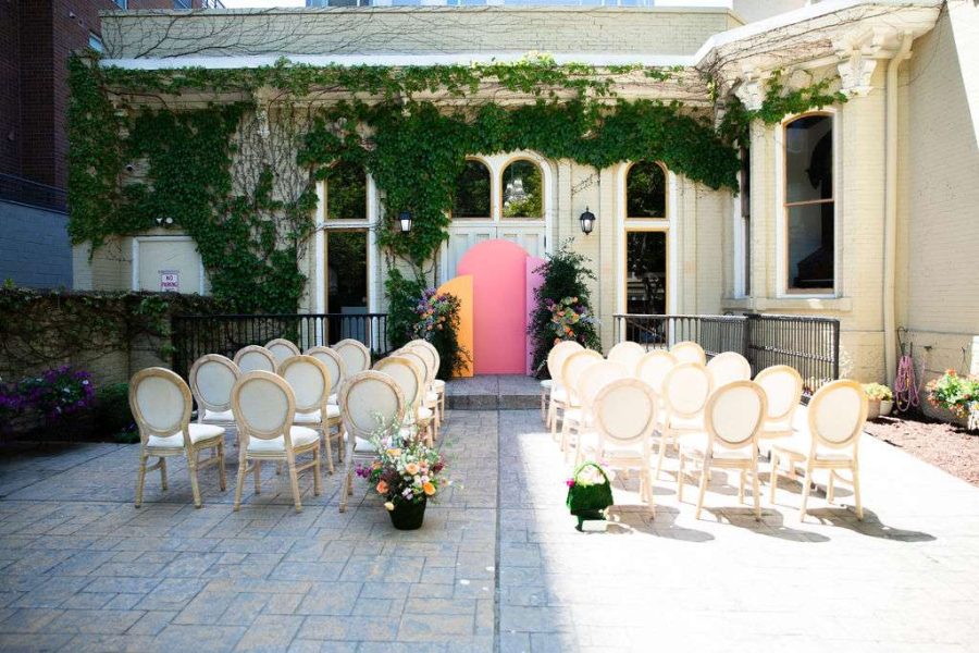 Outdoor ceremony space at The Fitzgerlad with colorful backdrop arches and white fabric chairs, ivy up the walls.