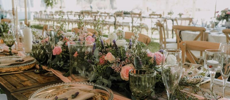 Wedding Table inspiration with large floral arrangement in pinks and greens. Chargers and clear dinner plates with green glassware.